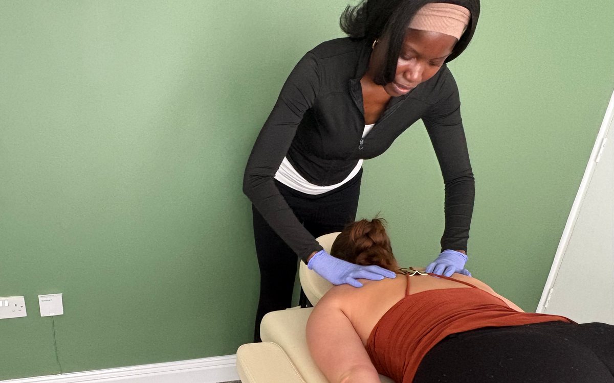 Deborah Orilabawaye giving hands-on treatment to the upper back of a patient lying on the treatment couch