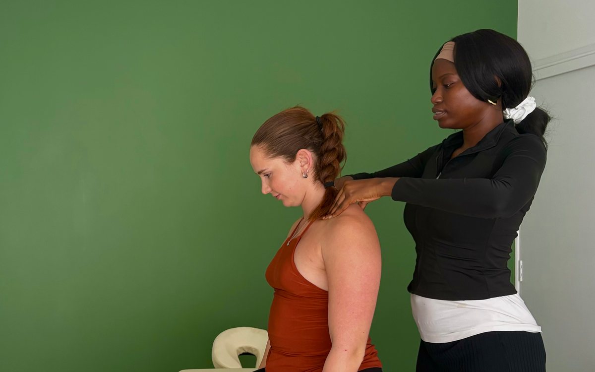 Deborah Orilabawaye assessing a seated patient's neck and shoulders in the treatment room